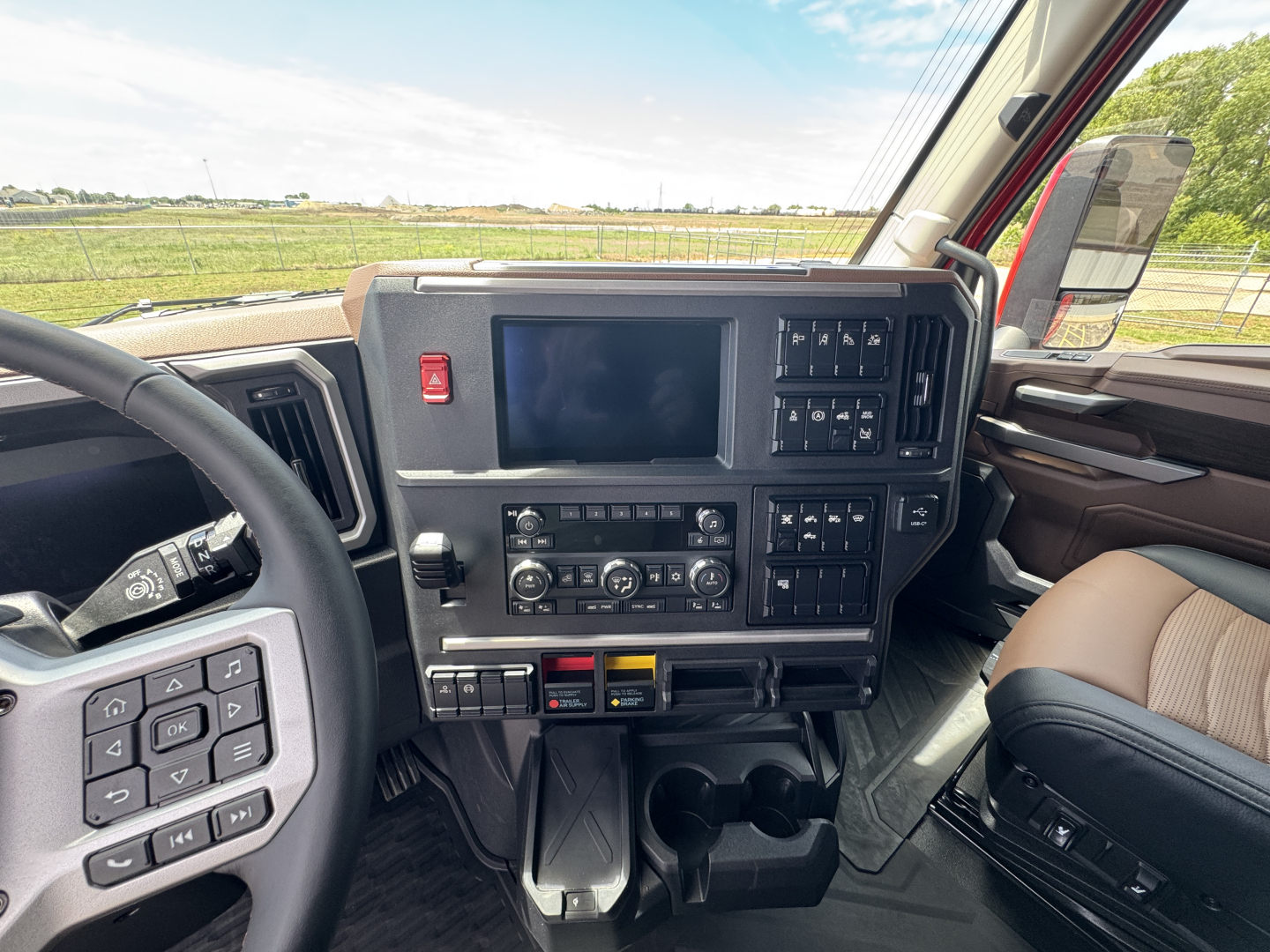 Truck cabin dash with touchscreen display and control panels in Mack PR64T76H, steering wheel left, center console, various switches and cup holders.
