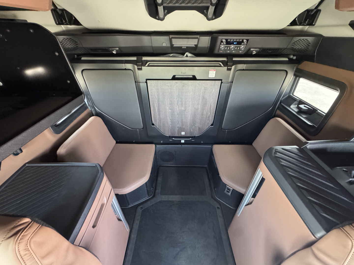 Truck interior cabin with front sleeper seating area, center cabinet, and dashboard; tan/brown upholstery and black panels visible.