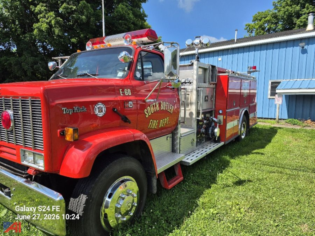 GMC Topkick 7000 pumper fire truck in red with ladder compartments, South Butler Fire Dept. logo on door, chrome fuel tanks, and emergency lights on cab roof.