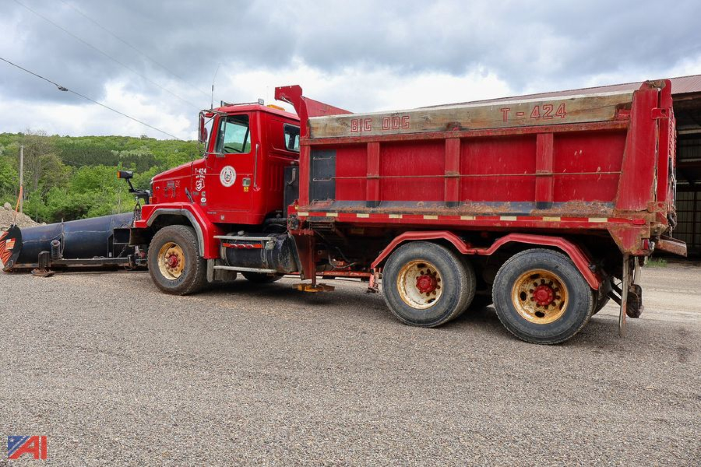 Dump truck side view showing red Volvo Autocar 6x4 dump-bed with plow attachment in front and gravel surface.