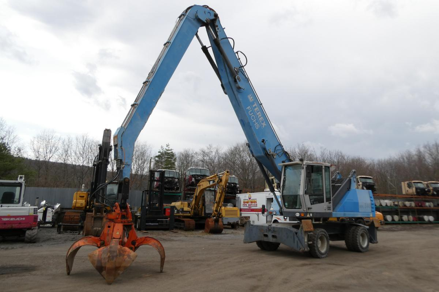 Telehandler boom arm raised over blue and gray Terex MHL340D with grappling attachment in a yard.