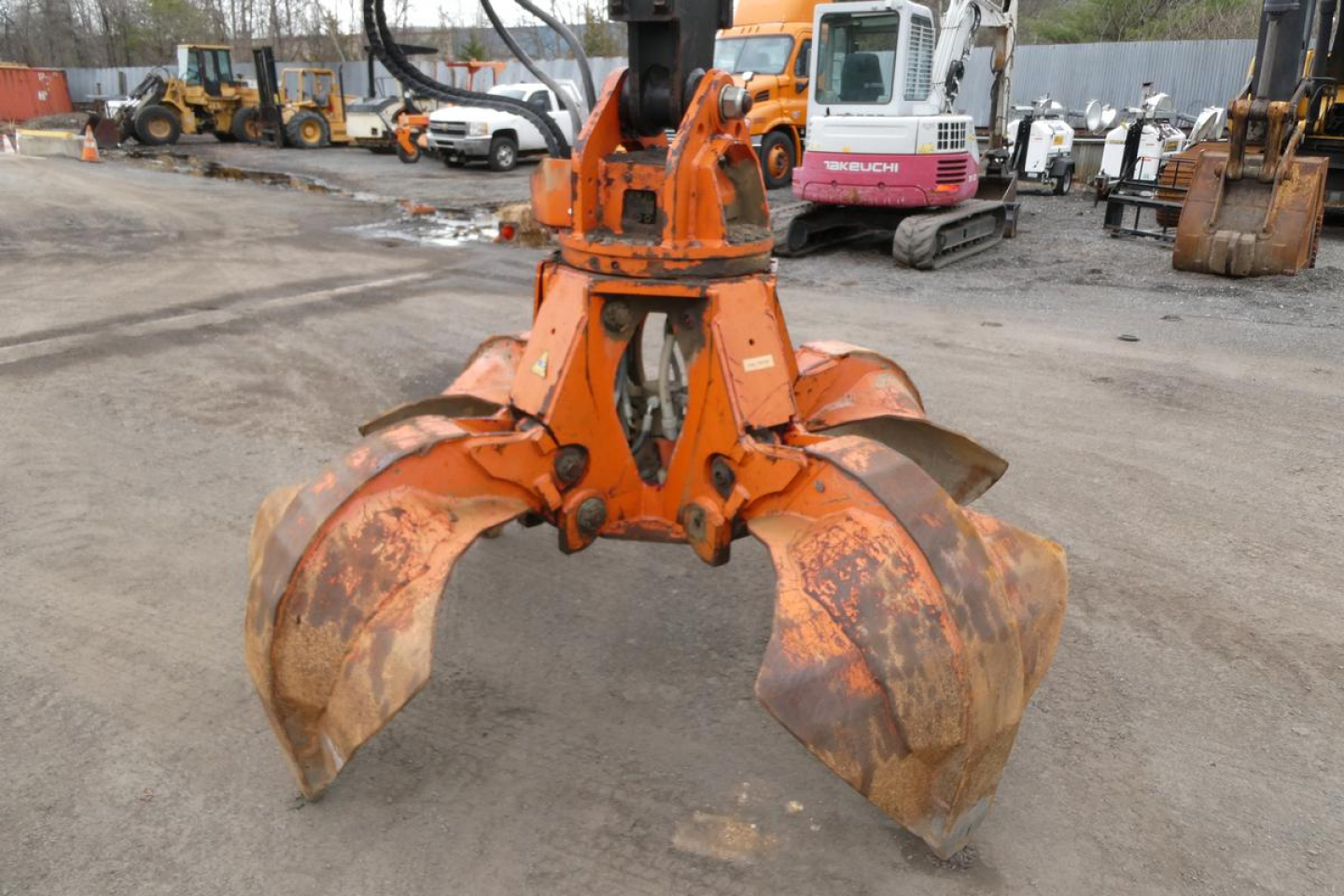 Terex MHL340D grapple attachment showing three large rust-colored clamshell jaws in a yard.