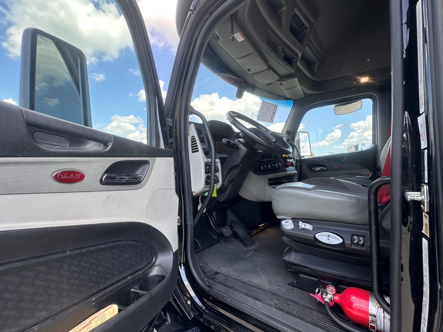 Truck cab interior of a 2022 Peterbilt 579, open driver door showing steering wheel, seat controls, dashboard, and Peterbilt logo on door panel.