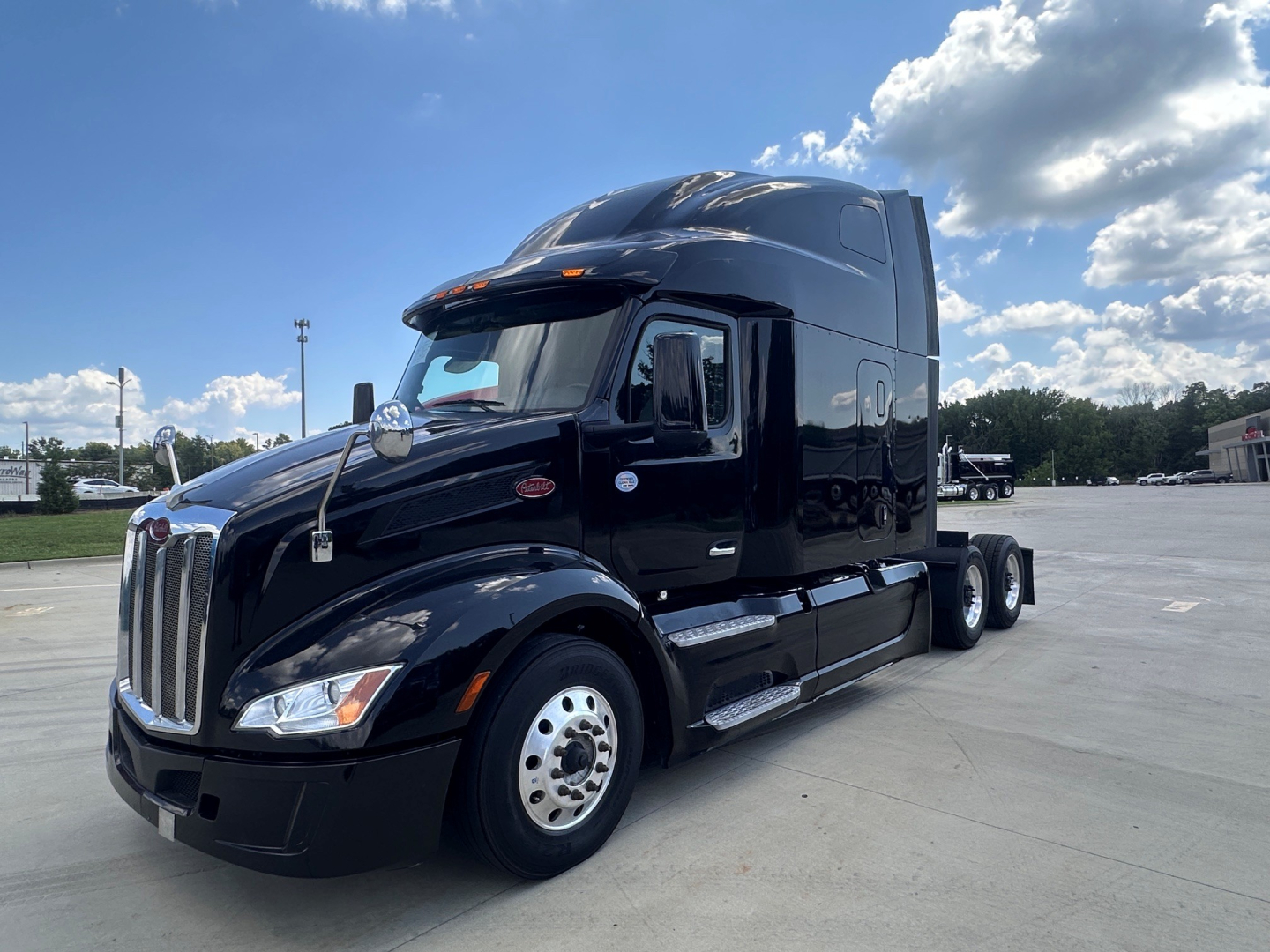 2022 Peterbilt 579 semi-truck tractor in a parking lot, black color, sleeper cab, side view with dual rear axles.