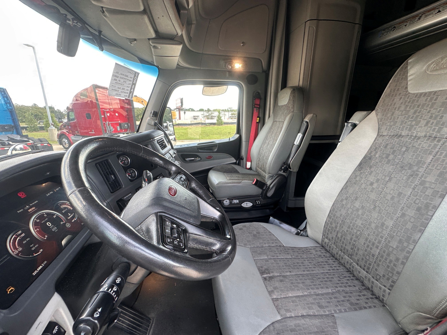 Peterbilt 579 truck cab interior with steering wheel, driver seat, and passenger bench visible; dashboard gauges and center console; light gray fabric seats.