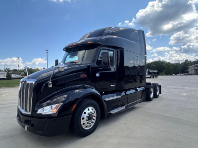 2022 Peterbilt 579 semi-truck tractor in a parking lot, black color, sleeper cab, side view with dual rear axles.