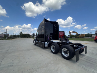 Peterbilt 579 tractor in a yard with sleeper cab, black paint, fifth wheel, dual rear axles, chrome rims.