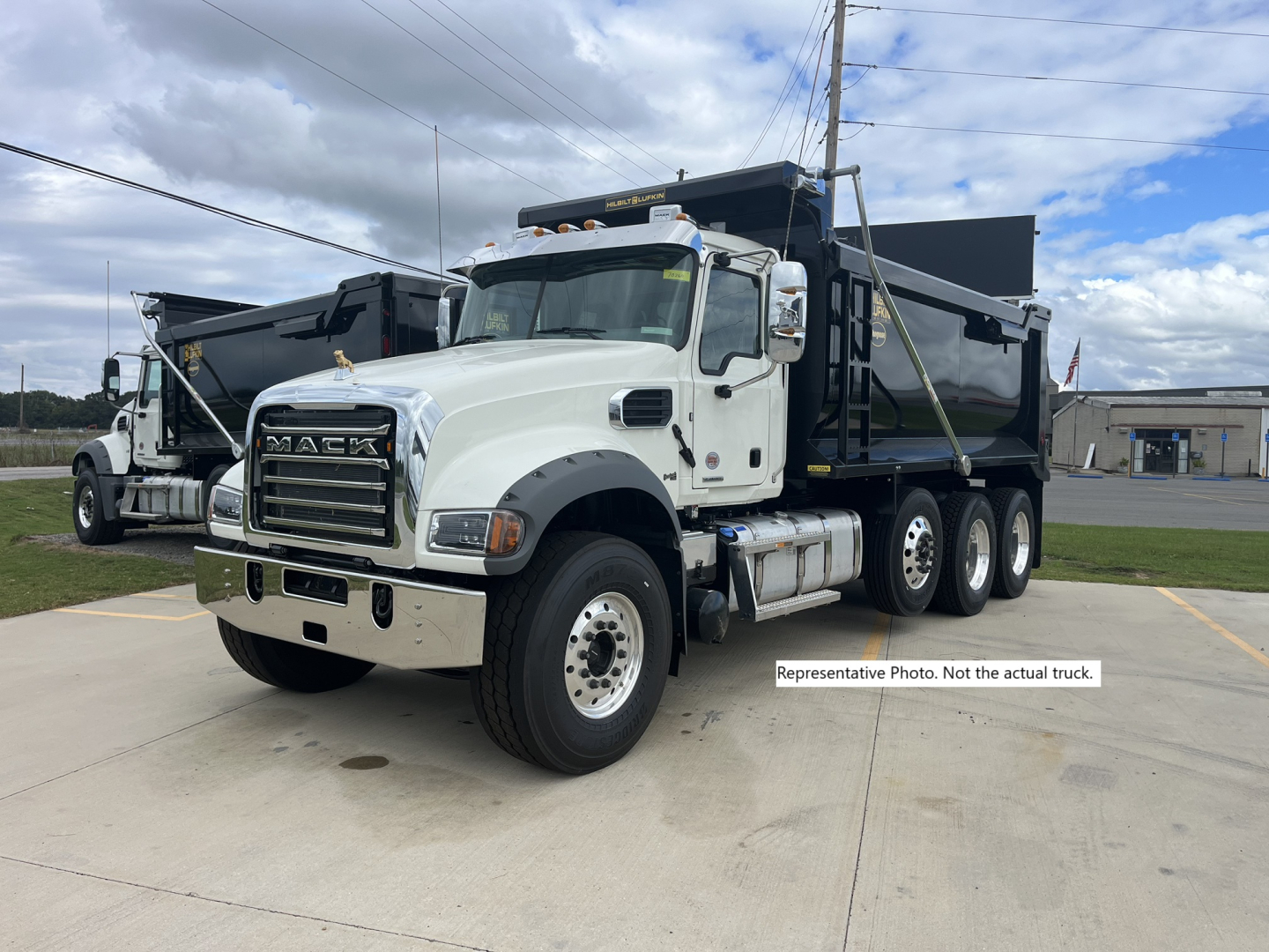 Mack dump truck in a parking lot showing front and side view with large chrome grille and black dump bed.