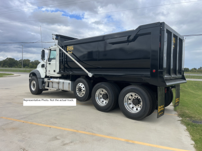 Dump truck showing Mack GR84F dump body and three axles with white cab and black bed.