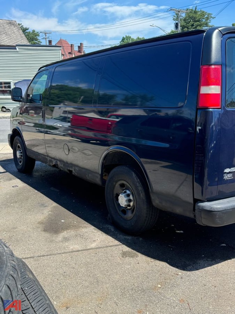 Chevrolet Express full-size van side/rear view showing dark blue body, passenger van, rear wheel and taillight, no visible windows on side panel.