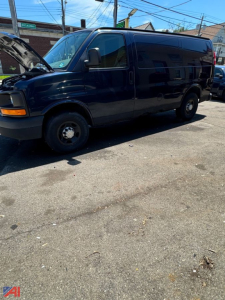 Rear-side view of a dark blue 2008 Chevrolet Express full-size passenger van with front hood open, showing side doors and wheel wells.