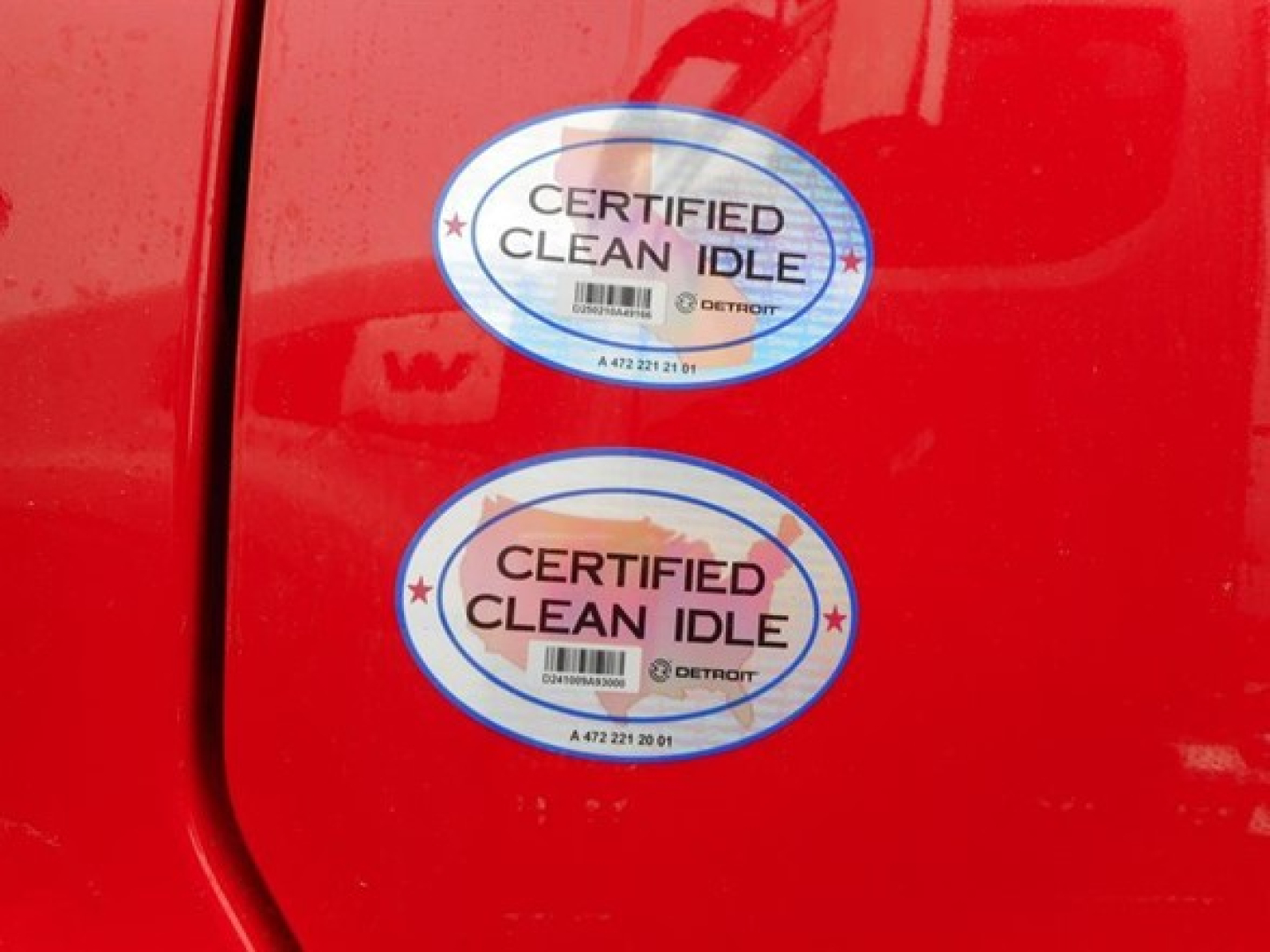 Two Certified Clean Idle stickers on a red Freightliner truck door showing Detroit logo and barcode.