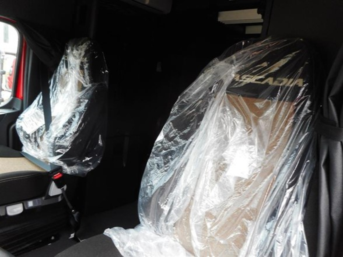 Truck cabin interior of a new Freightliner Cascadia 126 with plastic-covered seats and visible branding. 