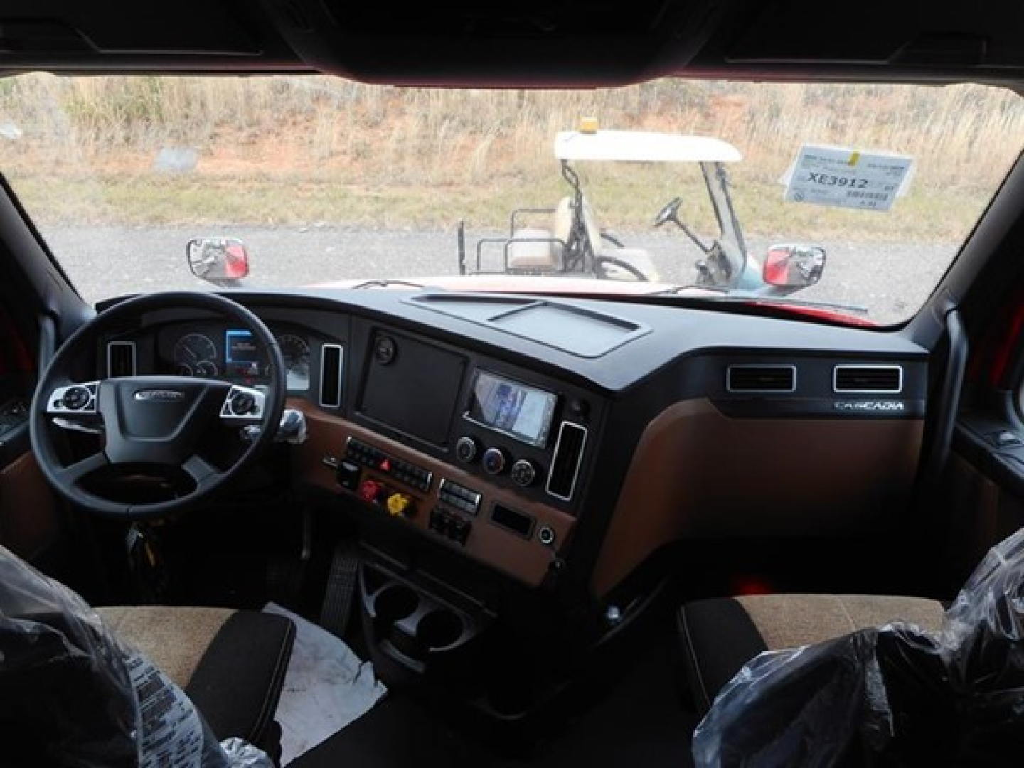 Cab interior of a new Freightliner Cascadia 126, viewing the dashboard, steering wheel, and center console with brown trim.