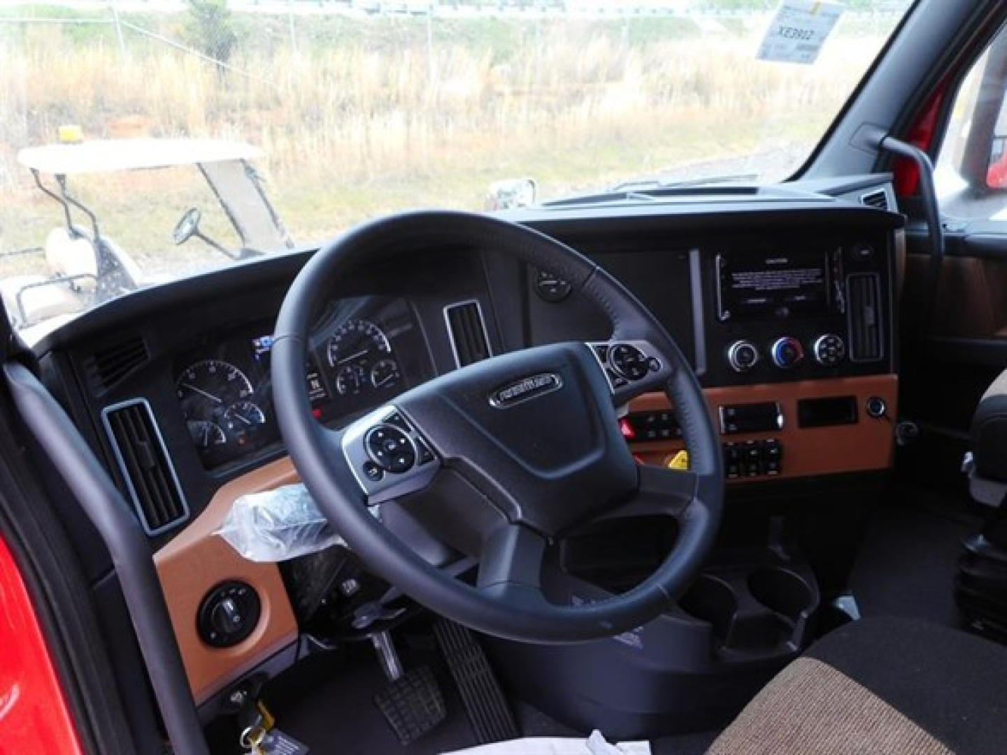 Freightliner Cascadia Cab interior showing steering wheel and dashboard with analog gauges and control panels.