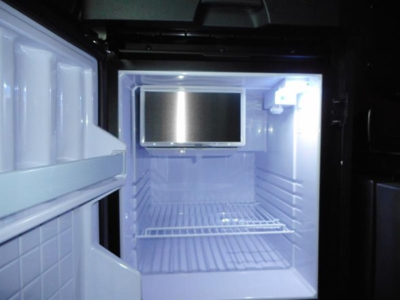 Freightliner Cascadia 126 truck interior fridge/freezer area with mounted monitor, showing a compact refrigerator unit and empty shelves.