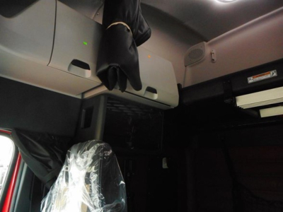 Cab interior of a 2027 Freightliner Cascadia 126 with overhead storage compartments and a plastic-covered driver seat, portion of dash and sleeper area visible.