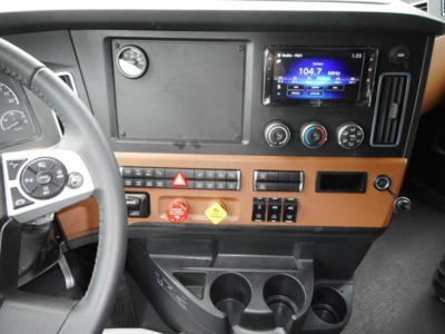 Freightliner Cascadia dash area showing steering wheel, infotainment screen, climate controls, hazard button, and cup holders in the cab interior