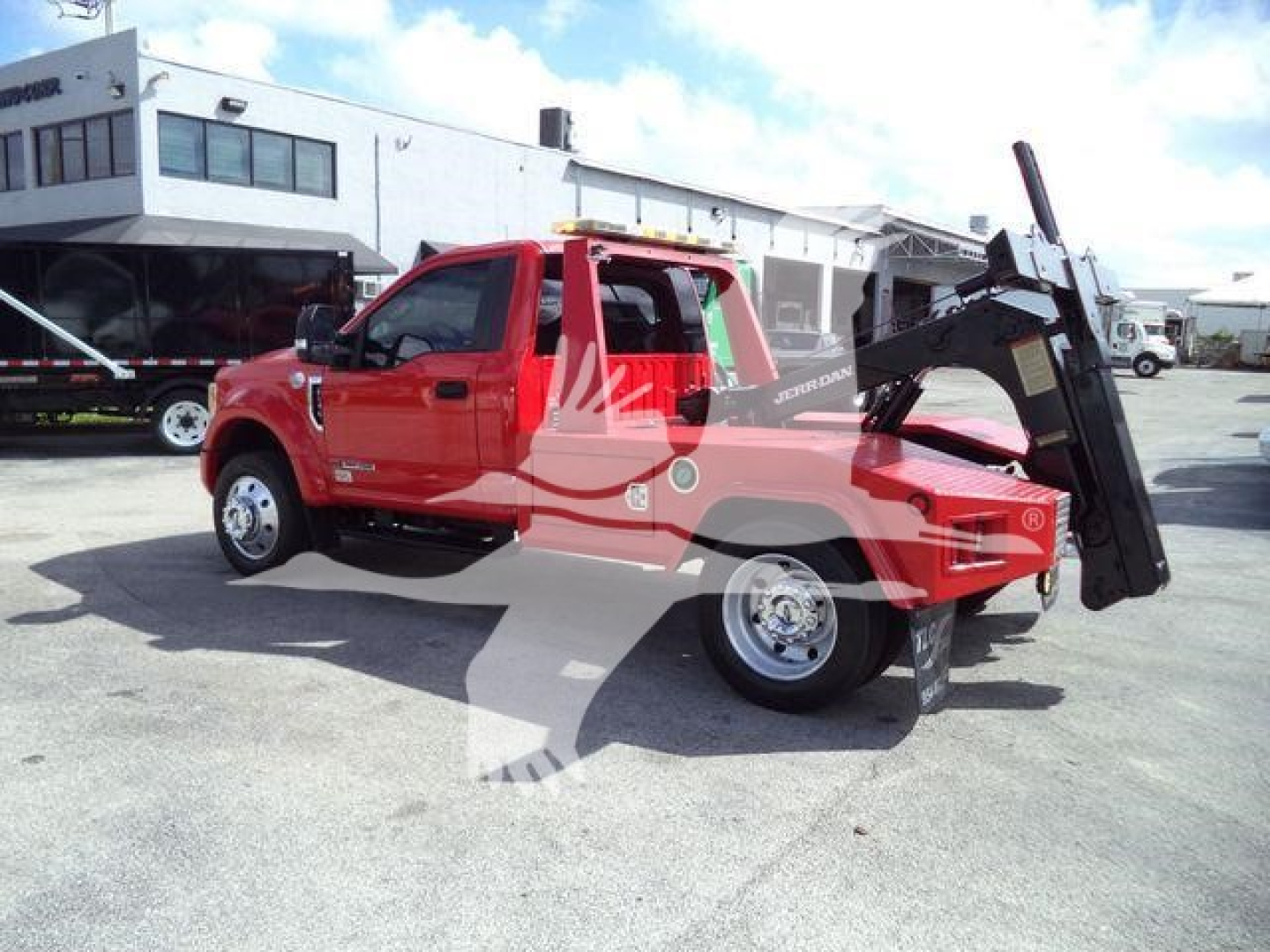 Ford F-450 XLT tow truck with a raised bed and hydraulic lift in a dealership lot.