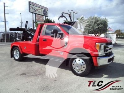 Ford F-450 tow truck with a bright red body in a dealership lot, flatbed with winch equipment visible.