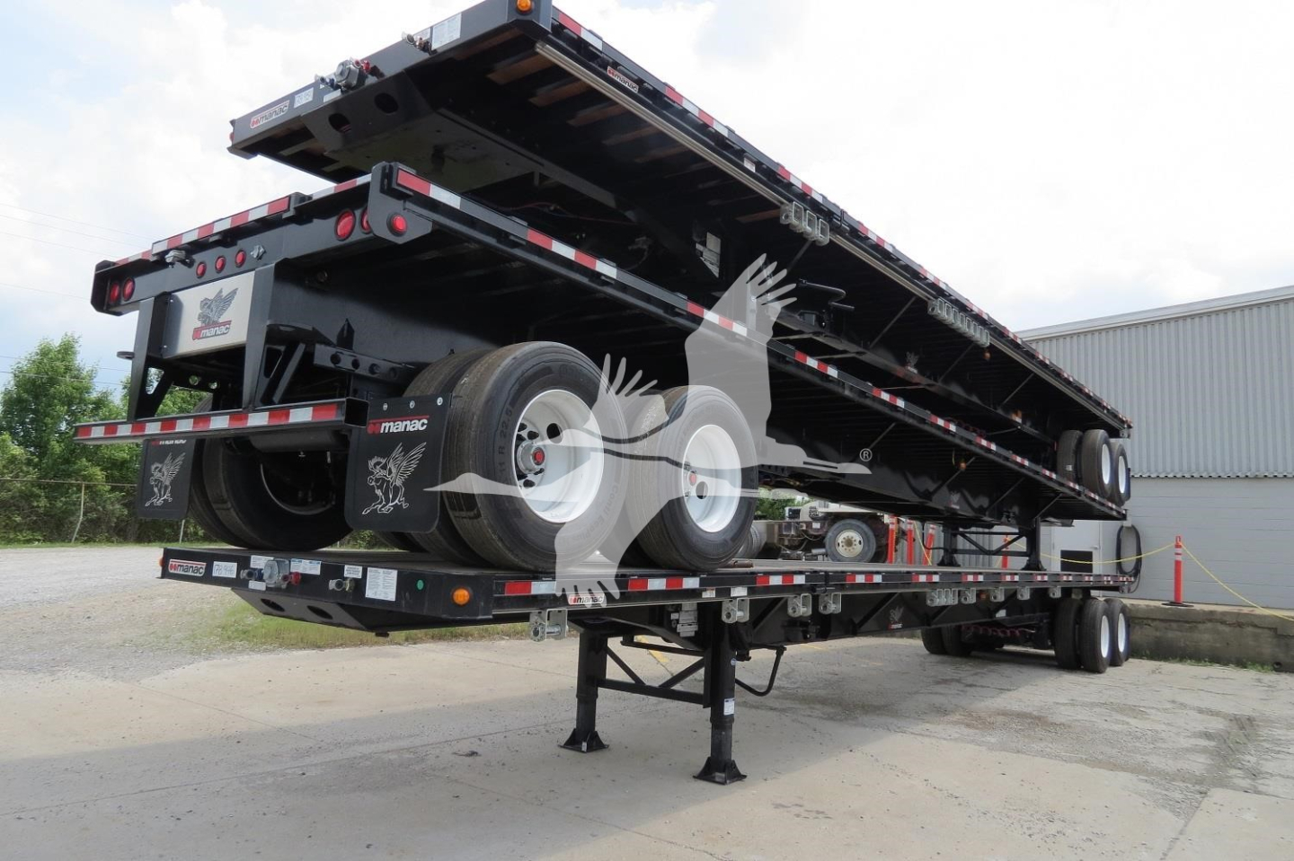 Manac extendable flatbed trailer in in-service condition with black frame, extendable deck, dual axles, and landing legs visible.