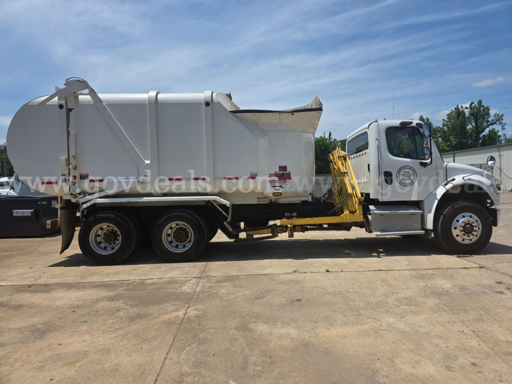 Freightliner M2 garbage truck side view showing rear compactor body and cab with yellow step platform.