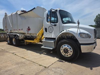 Freightliner M2 front-right side view showing white cab, garbage truck body, and loading mechanism with yellow lift arm; company logo on door and warning decals visible.