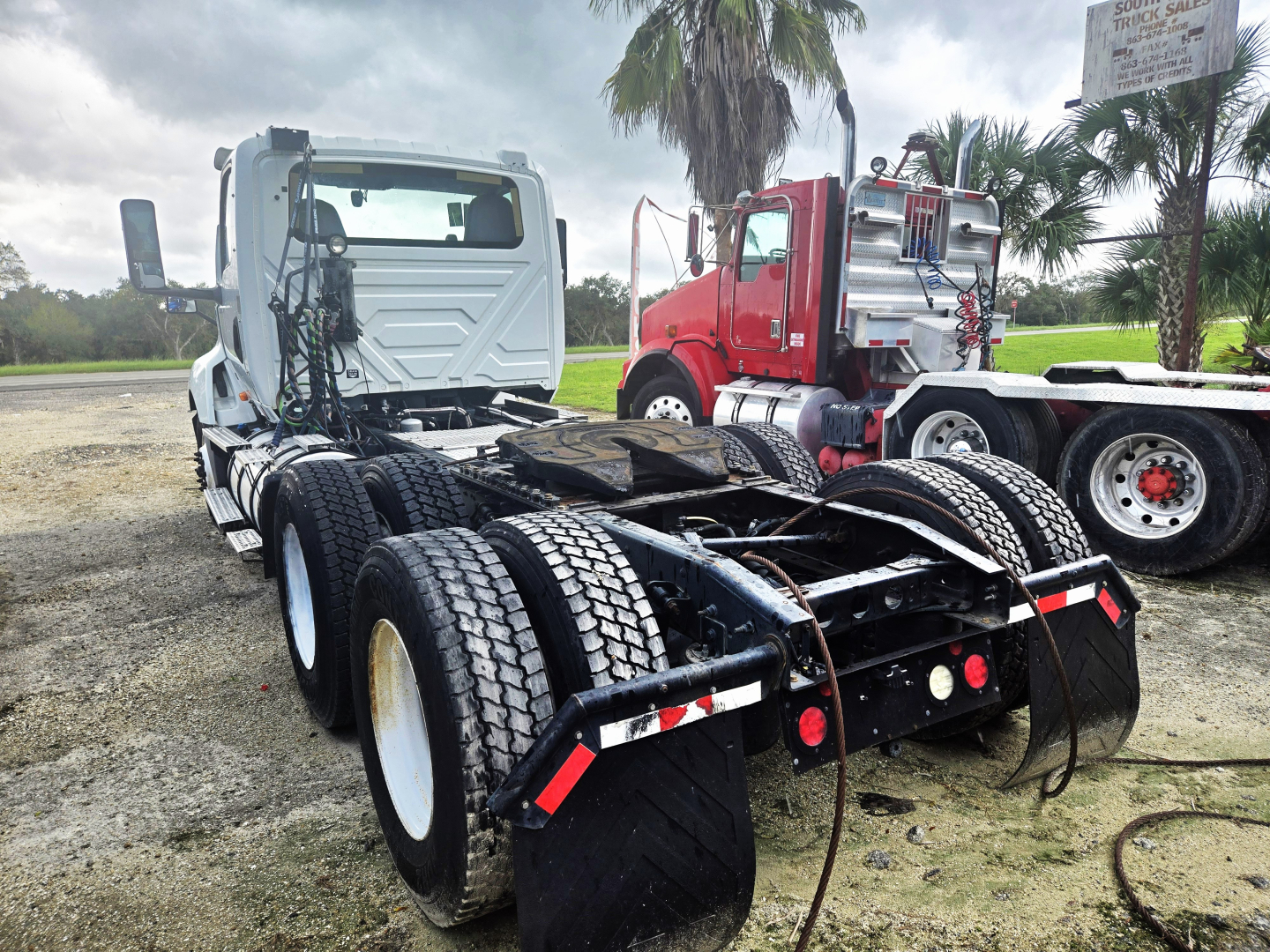 Truck chassis and cab viewed from rear with dual rear axles, International LT625 daycab, Cummins engine, heavy-duty tires, red and gray trucks in background.
