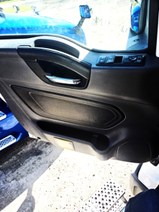 Truck cab interior door panel view showing window controls and door handle, with blue exterior seen at edge.