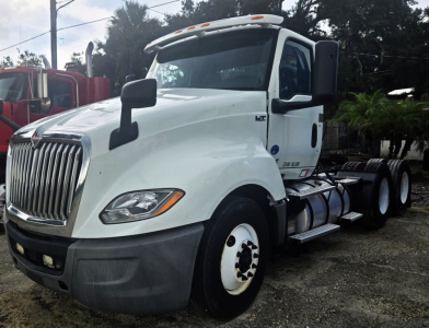 Truck cab showing International LT625 daycab with Cummins engine; white exterior, front grille, dual rear axles, side steps, and fuel tanks.
