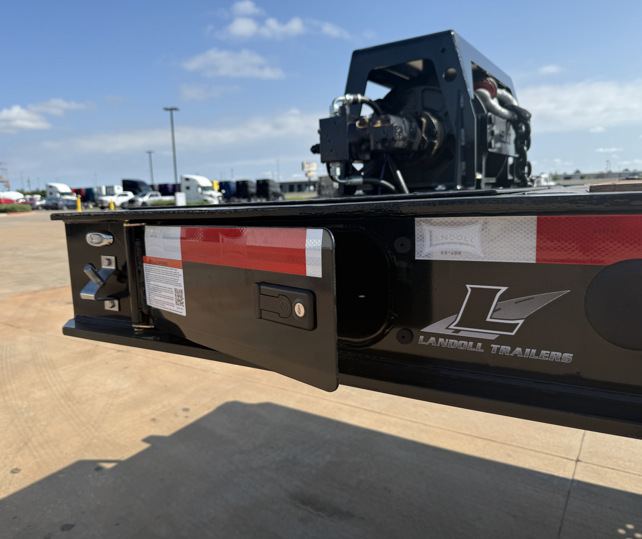 Landoll trailer rear showing L-Brand logo, reflective tape, and bumper plate with winch assembly in the background.