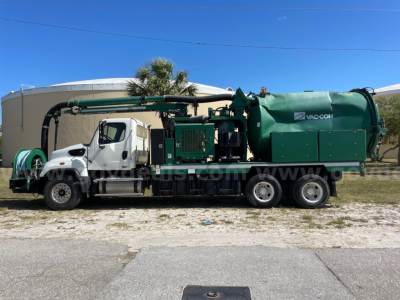 Freightliner 114SD vacuum truck with green vacuum tank and white cab, side view showing pump arm and hoses.