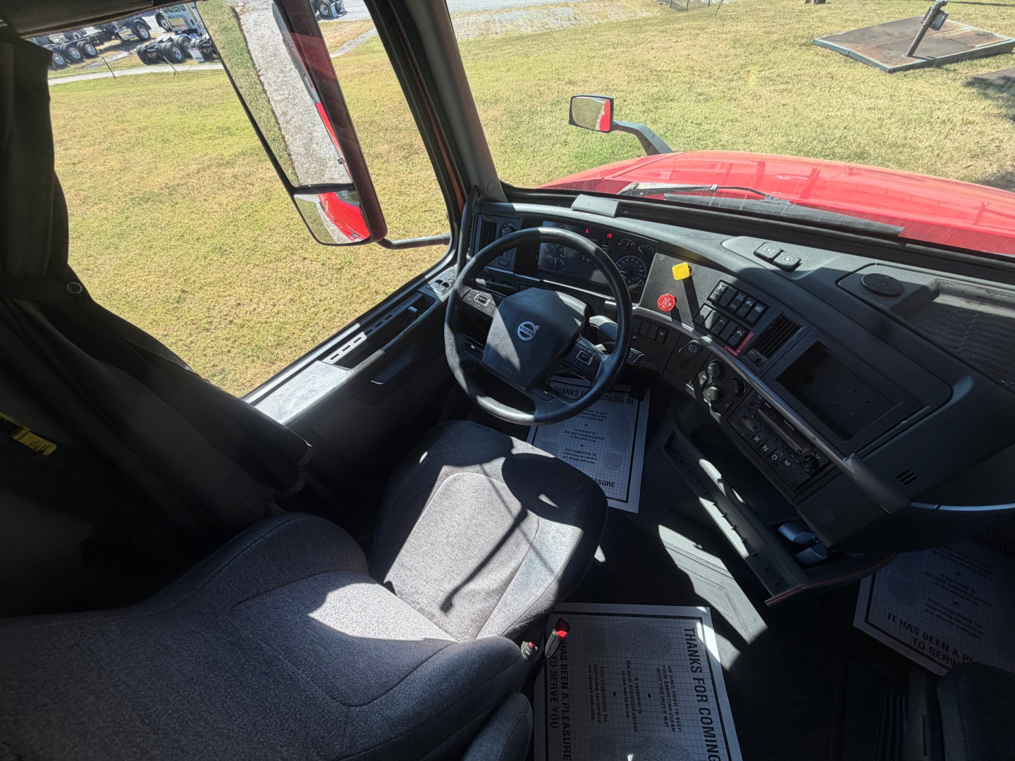 Volvo VNL truck cabin interior showing steering wheel, dashboard, and driver seat from passenger side perspective.