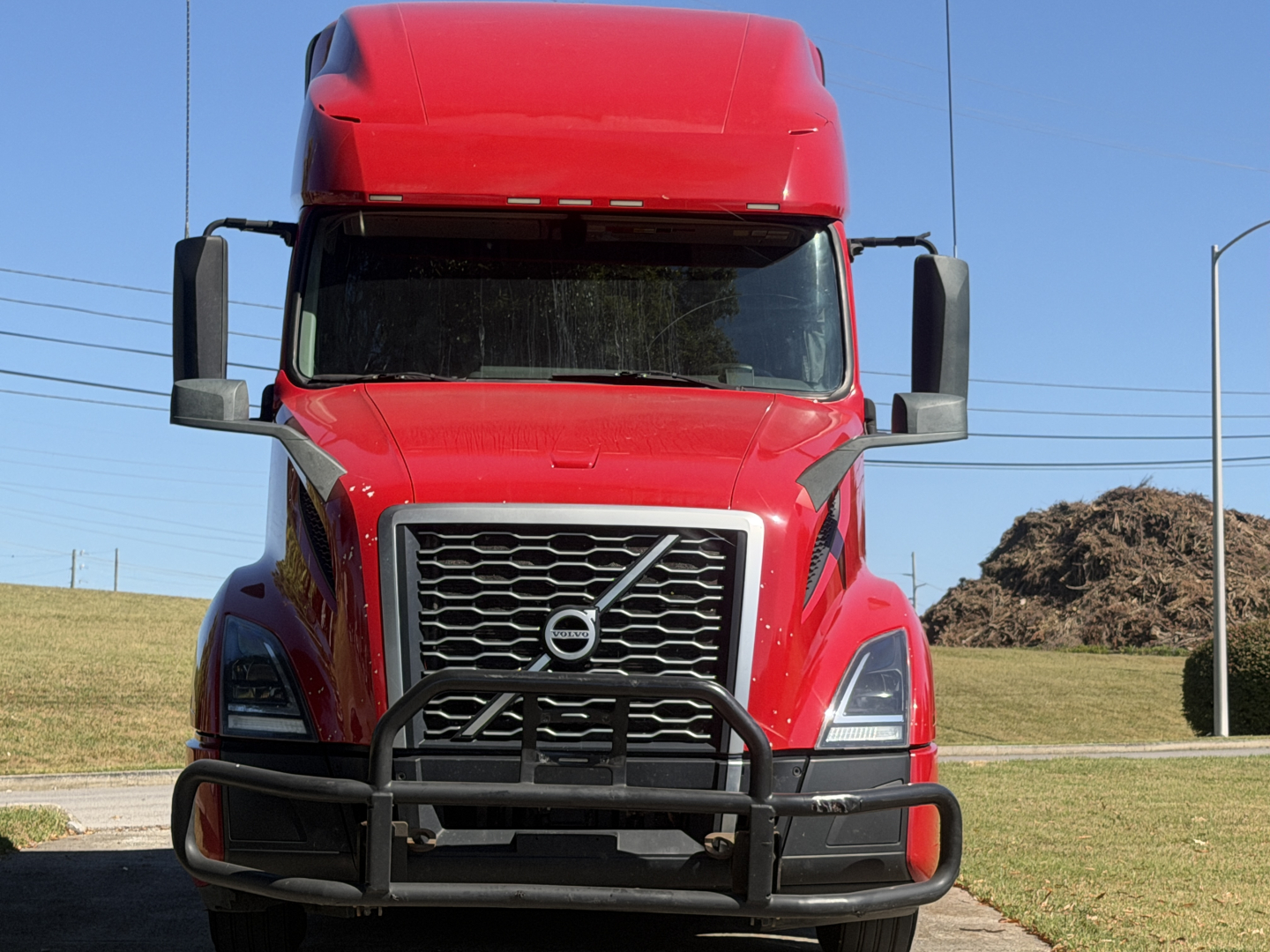 Volvo VNL64T760 truck front view showing bold grille, large bumper guard, red exterior, side mirrors, and windshield.