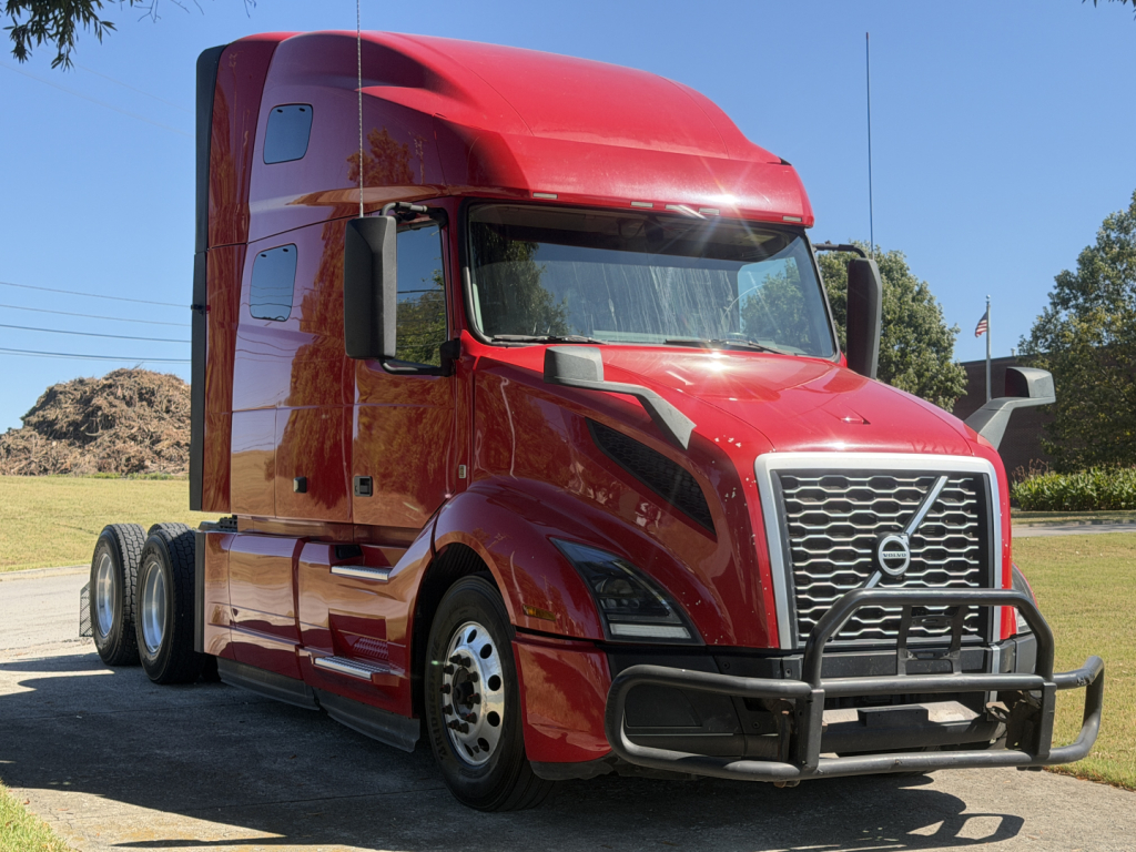Volvo VNL64T760 highway sleeper tractor in red, front grille with guard, large side mirrors, three rear axles, standard daylight.