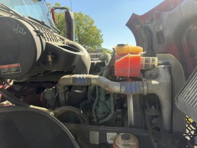 Volvo VNL64T760 engine bay view with fluid reservoirs and hoses visible, orange coolant/umm container, battery area, and surrounding components.