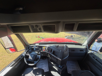 Interior of 2022 Volvo VNL64T760 cab showing steering wheel, dashboard, and driver seat with papers on the floor mats.