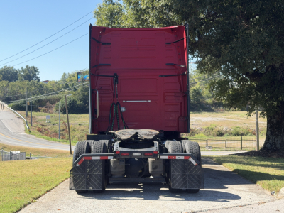 Rear view of a Volvo VNL64T760 truck tractor showing twin rear axles and fifth wheel, with red sleeper cab doors raised, in a parking lot.