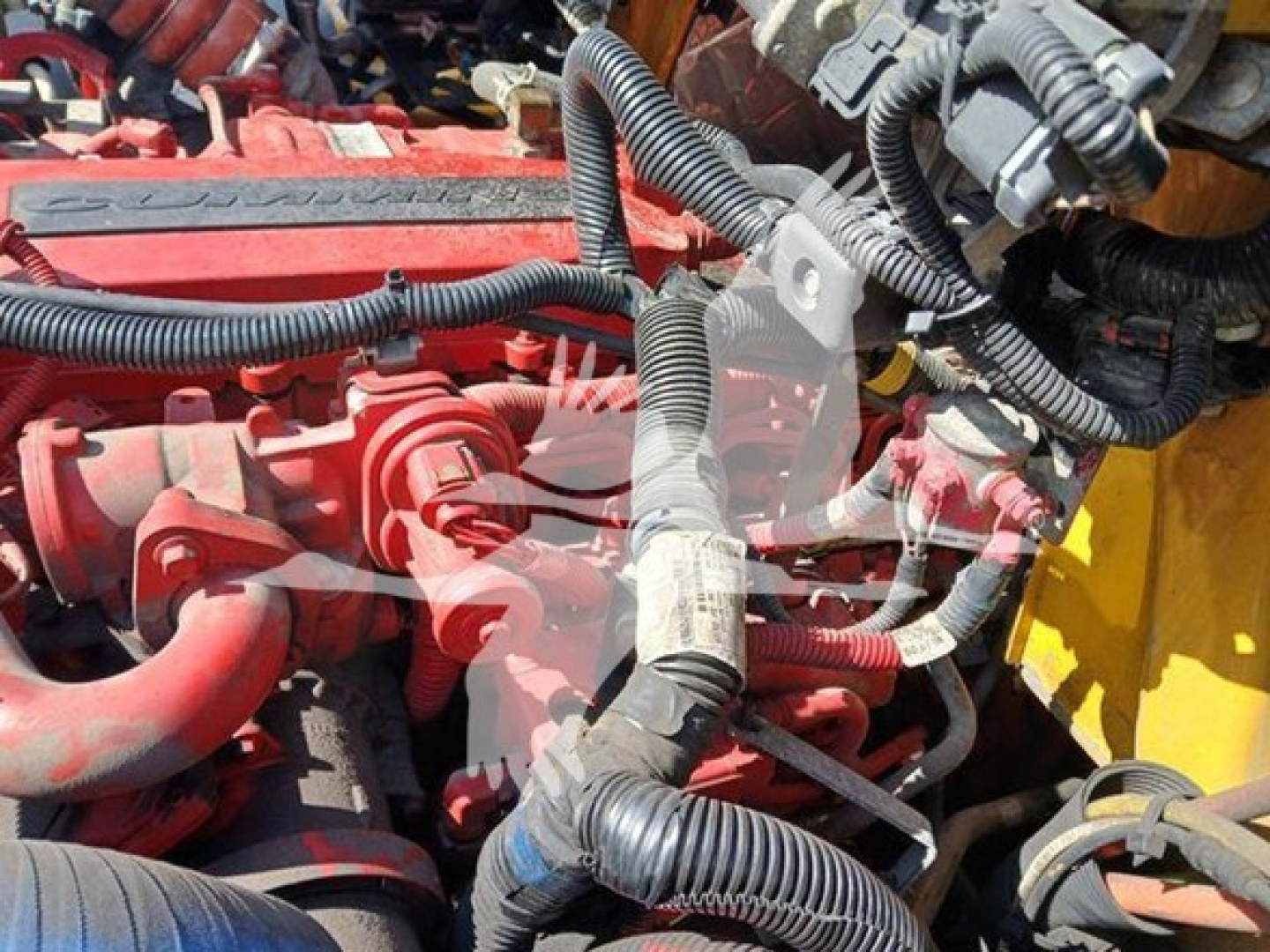 International MV engine bay showing red engine components, hoses, wiring harnesses, and a yellow painted surrounding structure.