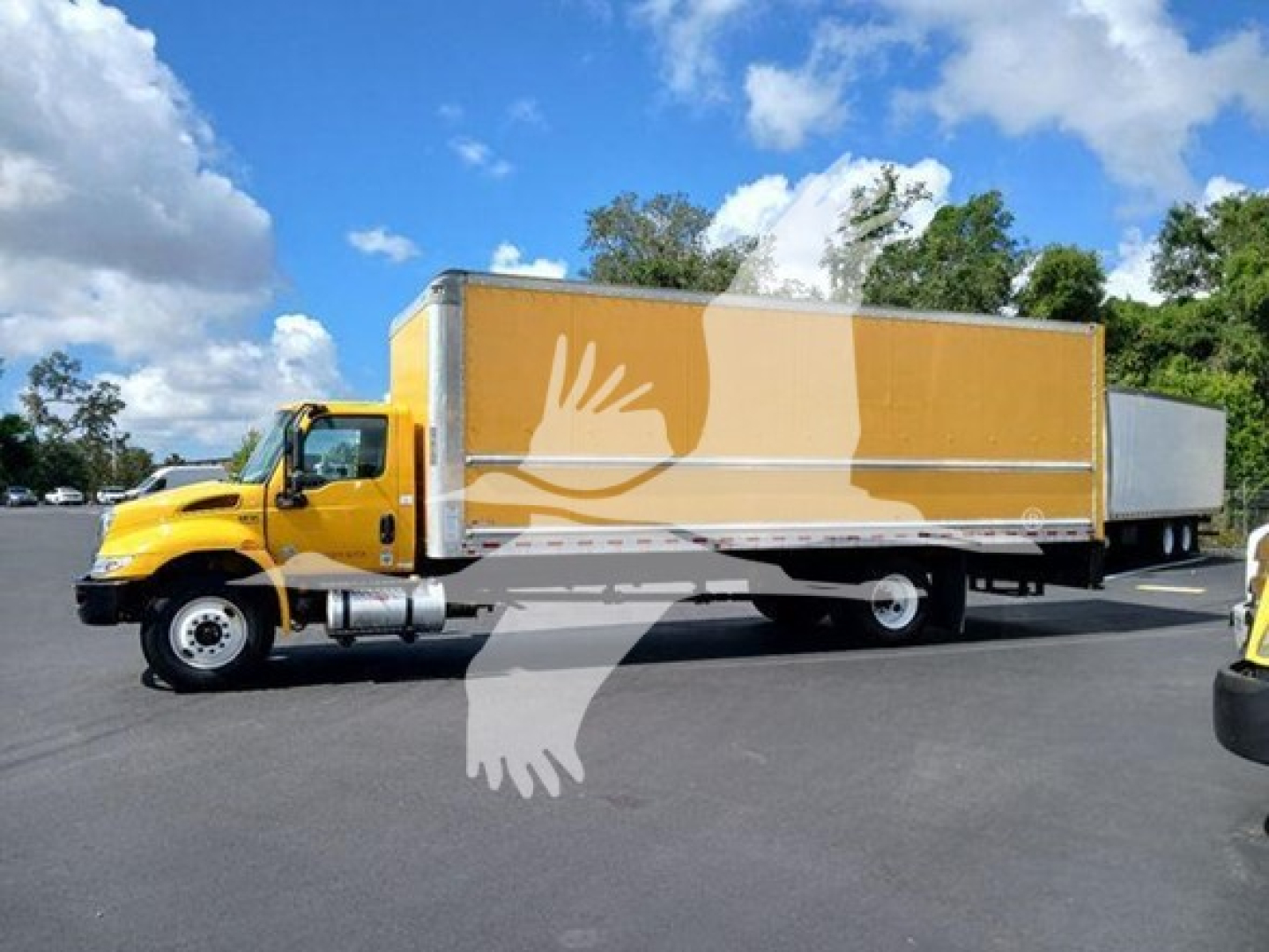 Truck mounted box truck with yellow cab and tan cargo box, side view showing large white graphic on box.