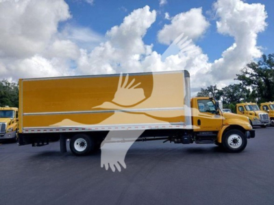Yellow box truck in a dealership lot with a long cargo box and cab, side view showing the entire box; no legible labels or text visible on truck side.