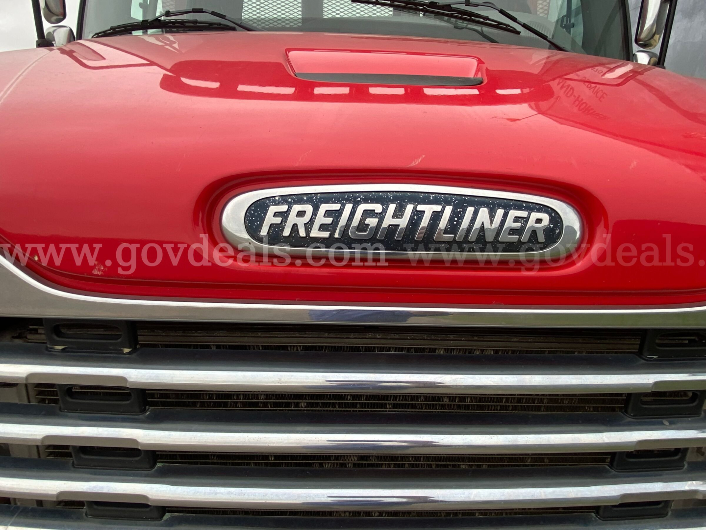 Front view of a red 2016 Freightliner M2 106 with chrome grille and emblem, hood reflection visible.
