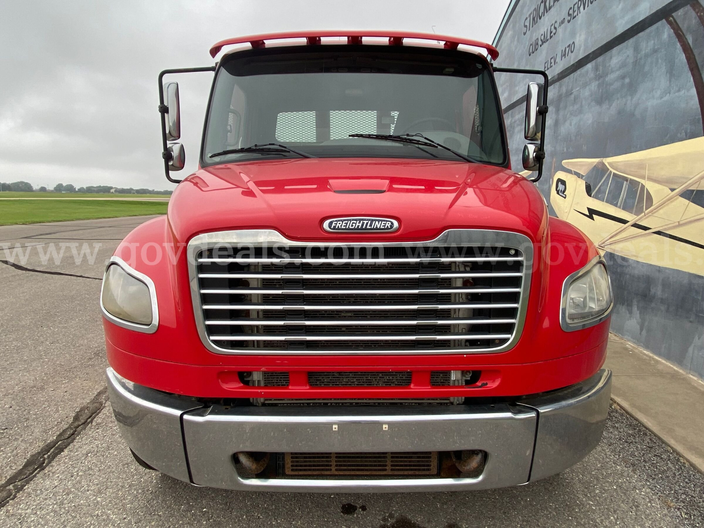 Front view of a red 2016 Freightliner M2 106 flatbed truck showing grille, headlights, bumper, and emblem.