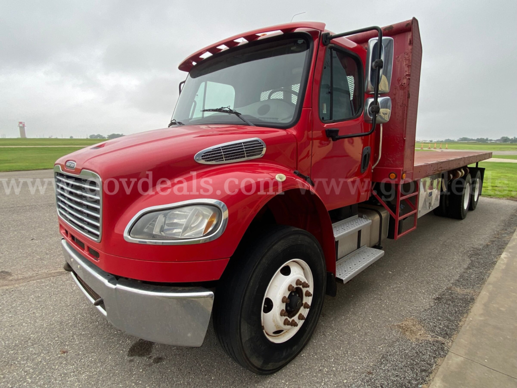 Freightliner M2 106 flatbed truck in red, front and passenger-side view, showing cab, chrome front bumper, grille, large side mirrors, and flatbed bed.