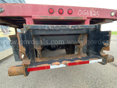 Rear view of a Freightliner M2 106 flatbed trailer hitch with rusted steel frame and bumper, showing rear axle and hitch assembly.