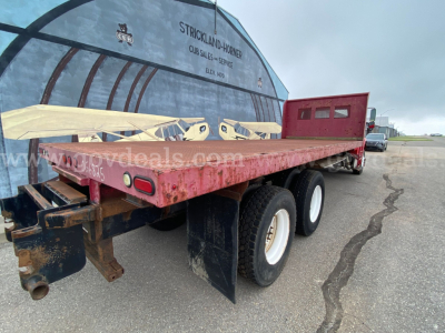 Flatbed trailer attached to Freightliner M2 106 chassis with dual rear wheels and red stake bed.