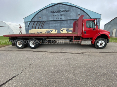 Flatbed truck with red cab and long flatbed, Freightliner M2 106, side view showing triple rear axles.