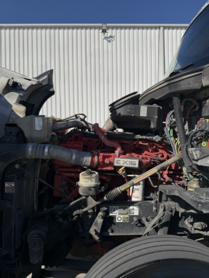 Kenworth T680 engine bay with red engine block, visible labels including 6XIS and various hoses and electrical wiring.