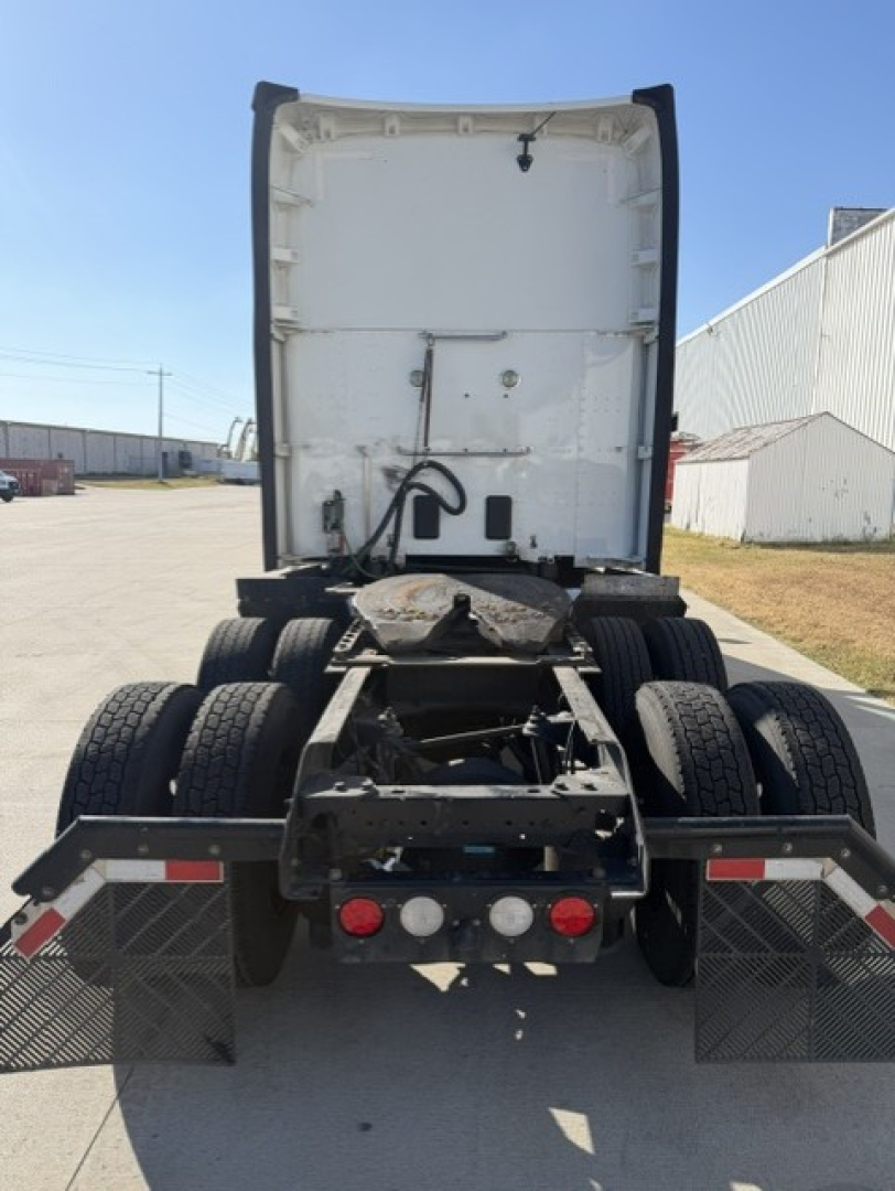 Kenworth truck rear view showing fifth wheel, dual rear axles, and mud flaps. Visible components include bumper lights, chassis, and white sleeper cab back panel.