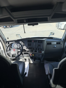Kenworth T680 interior from driver’s seat, steering wheel, dashboard, gauges visible; windshield and mirror views ahead; cab layout with controls and seating.